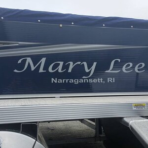 K&ouml;nnte beinhalten: Ein blaues und silbernes Pontonboot mit dem Namen "Mary Lee" und dem Ort "Narragansett, RI" auf der Seite.