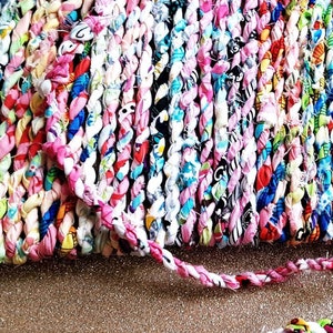 May include: A close-up of a colorful braided rope made from fabric scraps. The rope is twisted and has a variety of patterns and colors, including pink, blue, white, and green.