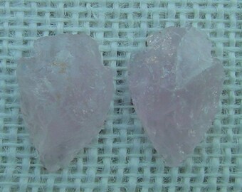 May include: Two pale pink, translucent, irregularly shaped crystals on a white woven background.