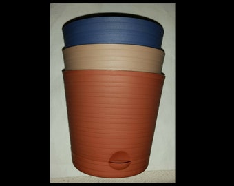 May include: Three plastic plant pots stacked on top of each other. The top pot is blue, the middle pot is beige, and the bottom pot is terracotta.