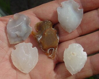 May include: Five arrowheads made of white and brown stone. The arrowheads are different sizes and shapes.