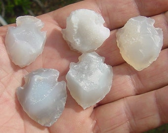 May include: Five white agate arrowheads with a translucent, milky appearance. The arrowheads are smooth and polished, with a slightly rough texture.