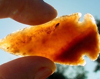 May include: A translucent orange arrowhead with a brown spot in the center, held up to the light.