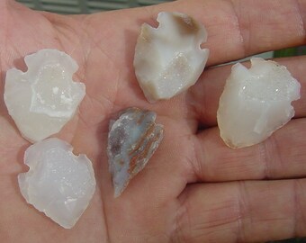 May include: Five arrowheads made of white agate with a crystalline texture. Some of the arrowheads have a brown or gray color variation.