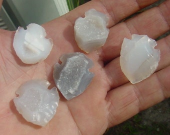 May include: Five white and gray agate arrowheads with a crystal-like texture. The arrowheads are in the shape of a traditional arrowhead with a point and two wings.
