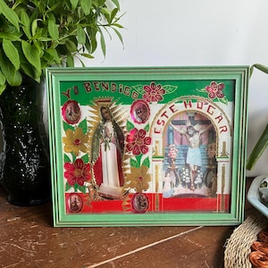 May include: A framed religious artwork with a green border. The artwork features images of religious figures, floral accents, and the text "YO BENDIGO ESTE HOGAR". The color palette includes red, gold, and green.