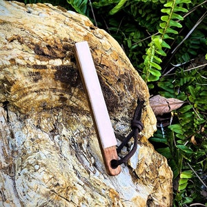 Puede incluir: Un pequeño iniciador de fuego rectangular blanco con un mango de madera marrón y una correa de cuero negro. El iniciador de fuego está apoyado en una gran roca erosionada.