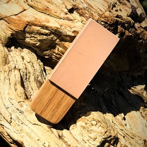 May include: A rectangular wooden block with a pink leather top. The block is resting on a piece of petrified wood.