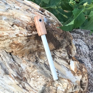 以下が含まれることがあります： 木製のハンドルが付いた小さな白い火起こし棒。ハンドルの上部に小さな穴があります。火起こし棒は化石化した木の塊の上に置かれています。