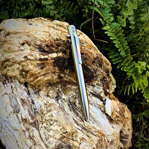 May include: A silver pen with a black clip and a red accent on a rough, brown, textured rock.
