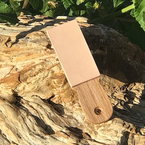 Puede incluir: Una piedra de afilar de cuero rosa claro con un mango de madera. La piedra de afilar se utiliza para afilar cuchillos.