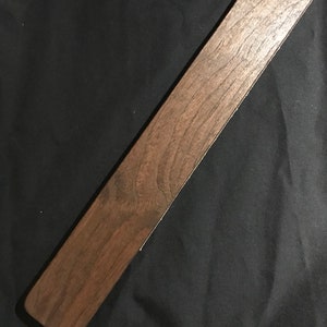 May include: A long, dark brown wooden paddle with a smooth, polished surface.