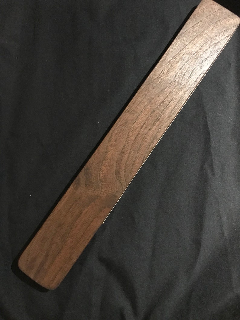May include: A long, dark brown wooden paddle with a smooth, polished surface.