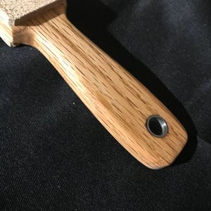 Puede incluir: Un mango de madera con un bloque de lija de cuero unido al extremo. El mango tiene un anillo de metal para colgar.