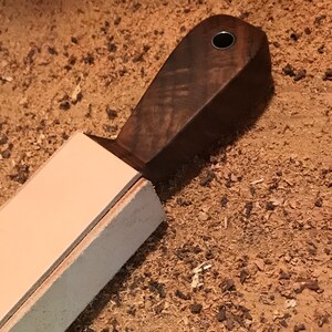 Peut inclure: Une strop en cuir brun clair avec une poign&eacute;e en bois brun fonc&eacute;. La poign&eacute;e a un petit trou en haut.