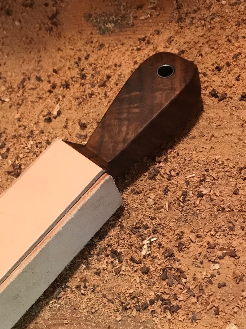 Peut inclure: Une strop en cuir brun clair avec une poign&eacute;e en bois brun fonc&eacute;. La poign&eacute;e a un petit trou en haut.