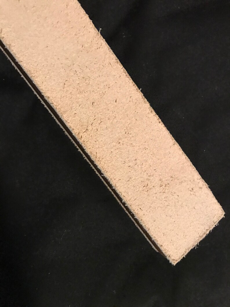 Puede incluir: Primer plano de una correa de cuero beige claro con textura rugosa. La correa est&aacute; sobre una superficie negra.