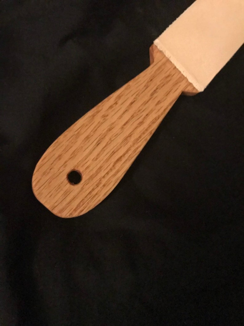 May include: A wooden strop with a leather strop attached to the top. The strop has a hole in the handle.