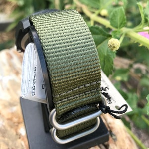 May include: A green and brown nylon watch strap with silver metal hardware. The strap is attached to a watch face that is not visible in the image.