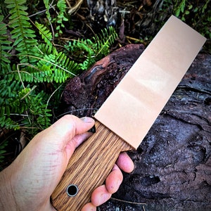 May include: A wooden handled leather strop for sharpening knives. The strop has a light brown leather surface and a dark brown wooden handle with a metal ring.