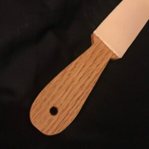 May include: A wooden handle with a hole in the centre and a light pink leather strop attached to the end.
