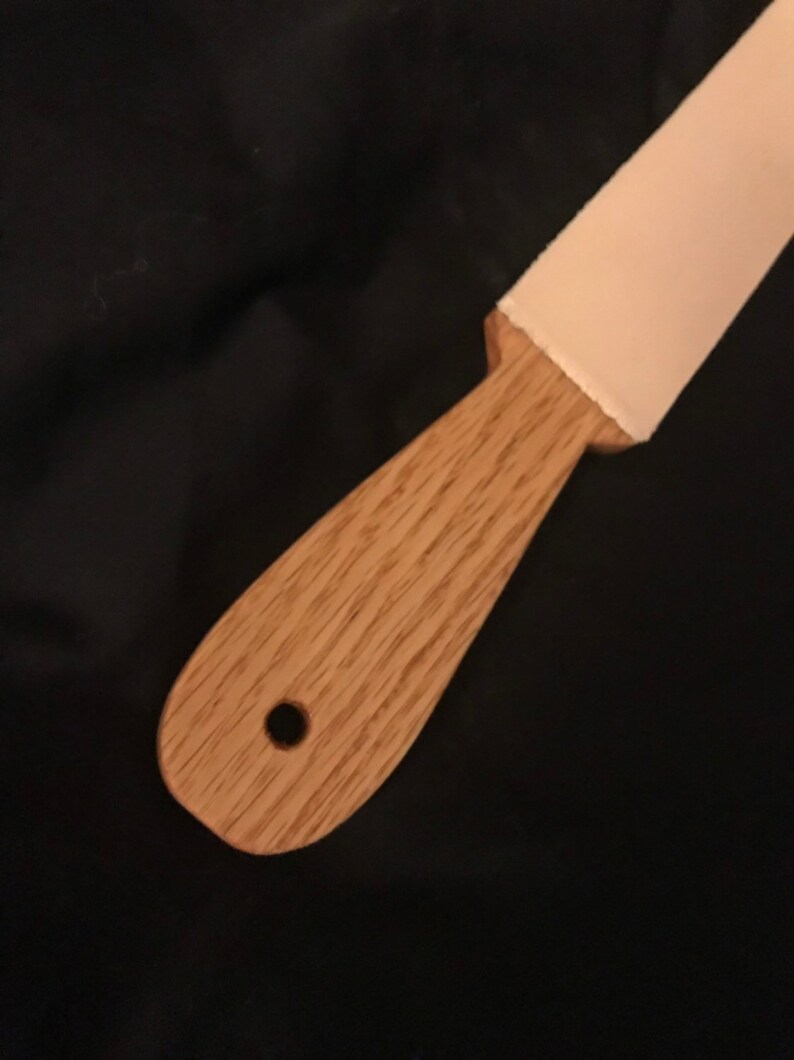 May include: A wooden handle with a hole in the centre and a light pink leather strop attached to the end.