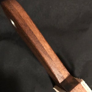 Puede incluir: Primer plano de un mango de cuchillo de madera con una mancha marr&oacute;n oscura. El mango est&aacute; hecho de dos tipos diferentes de madera, una clara y otra oscura.