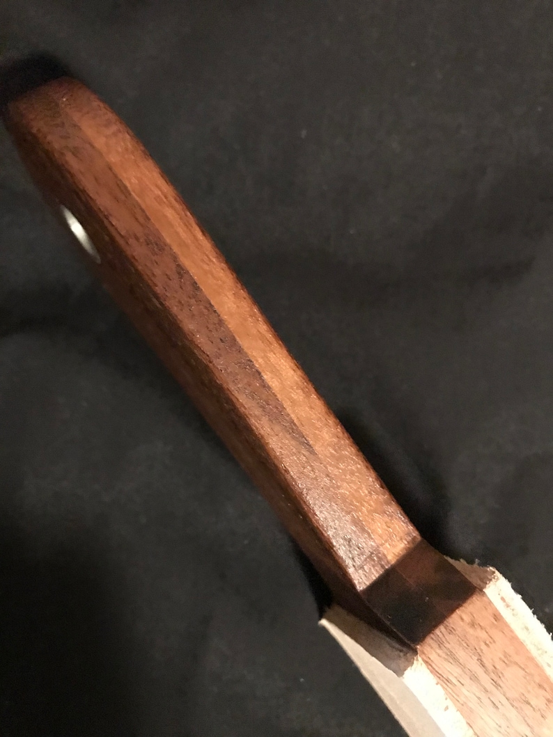 Puede incluir: Primer plano de un mango de cuchillo de madera con una mancha marr&oacute;n oscura. El mango est&aacute; hecho de dos tipos diferentes de madera, una clara y otra oscura.