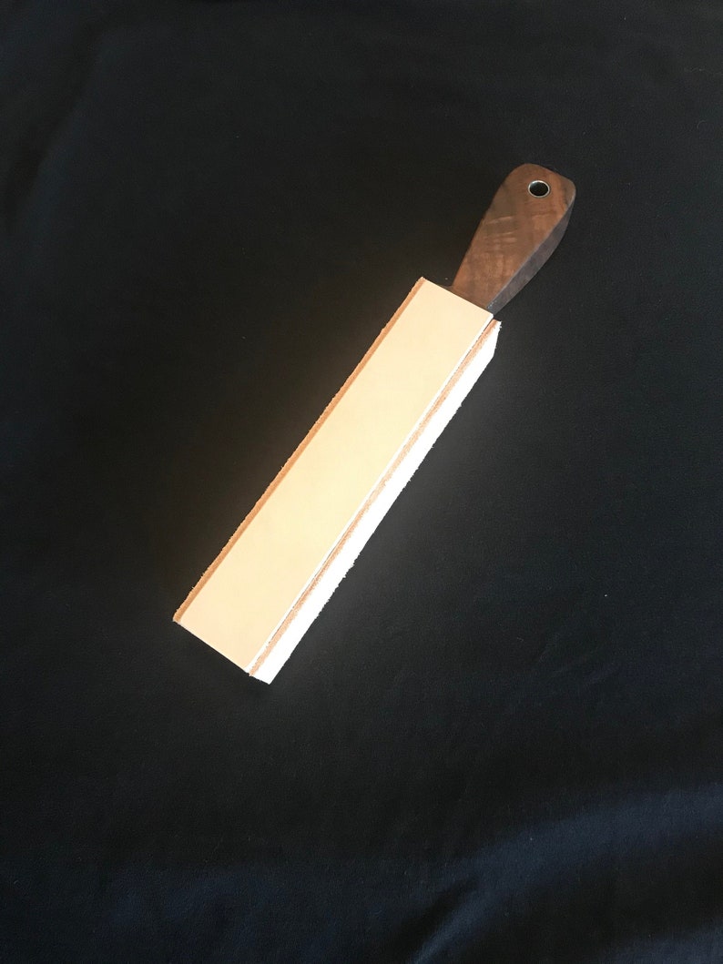 Peut inclure: Une strop en cuir brun clair avec une poign&eacute;e en bois brun fonc&eacute;. La strop est utilis&eacute;e pour aiguiser les rasoirs droits.