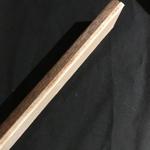 May include: A close-up of the edge of a wooden board with a light brown finish. The board has a smooth surface and a slightly rounded edge.
