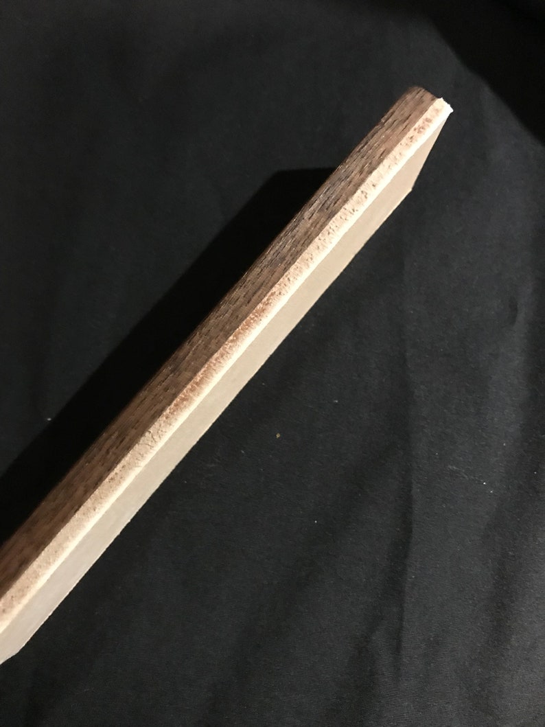 May include: A close-up of the edge of a wooden board with a light brown finish. The board has a smooth surface and a slightly rounded edge.