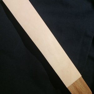 May include: A light brown leather strop with a wooden handle. The strop is used for sharpening straight razors.