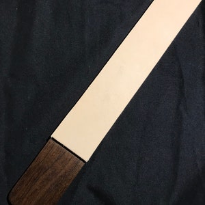 May include: A long, rectangular leather strop with a light beige color and a dark brown wooden handle.