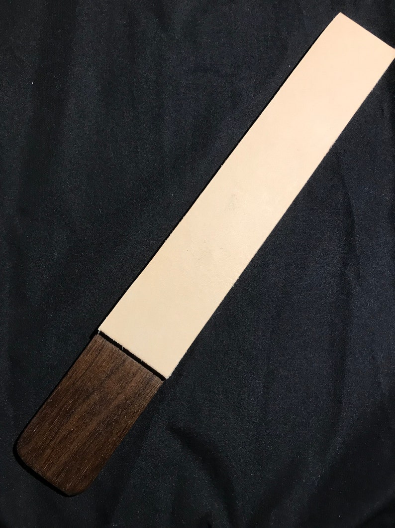 May include: A long, rectangular leather strop with a light beige color and a dark brown wooden handle.