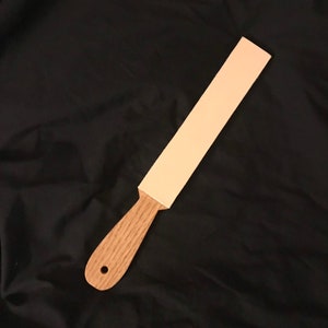 May include: A light brown wooden strop with a light pink leather strop surface.