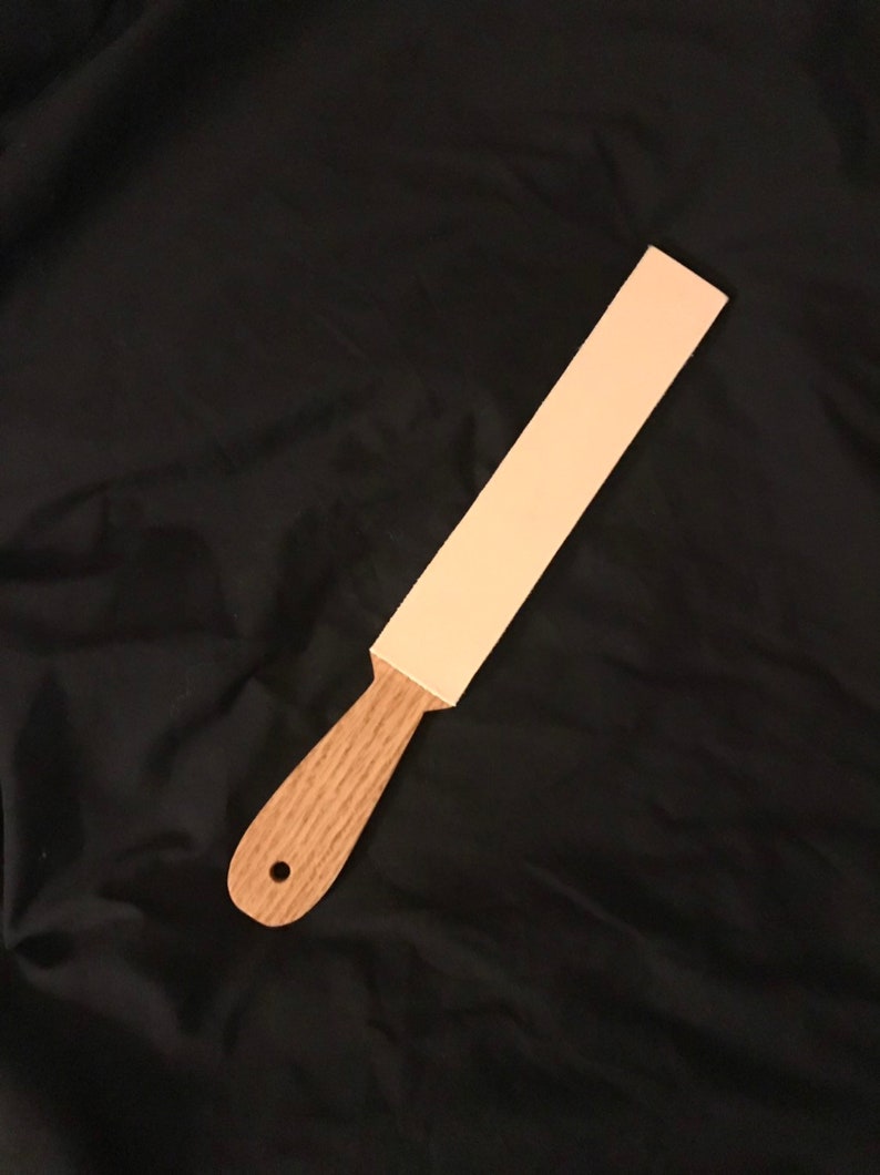 May include: A light brown wooden strop with a light pink leather strop surface.