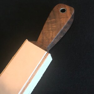 Peut inclure: Une strop en bois brun avec une sangle en cuir fix&eacute;e au sommet. La strop a un trou dans la poign&eacute;e.