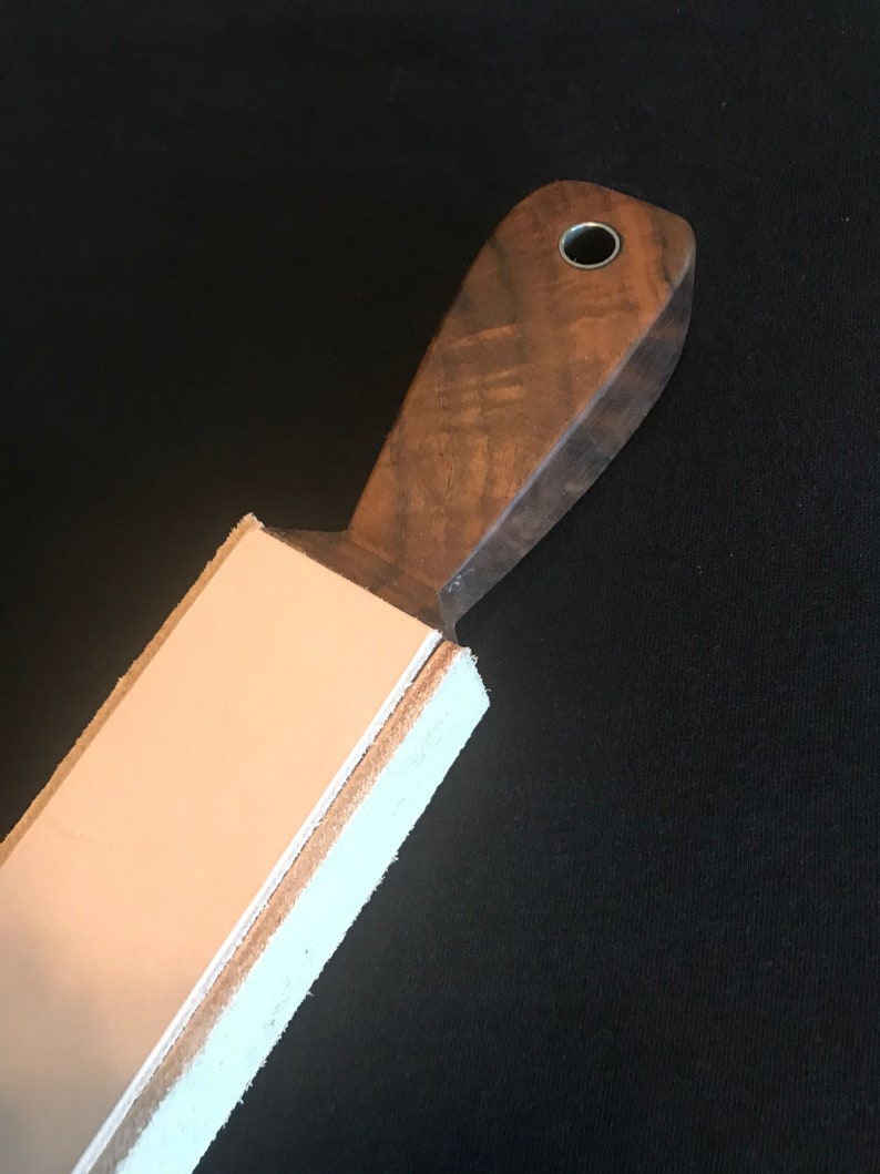 Peut inclure: Une strop en bois brun avec une sangle en cuir fix&eacute;e au sommet. La strop a un trou dans la poign&eacute;e.