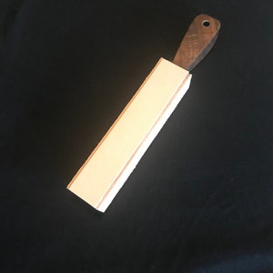 Peut inclure: Une strop en cuir blanc avec une poign&eacute;e en bois. La strop est utilis&eacute;e pour aiguiser les rasoirs droits.