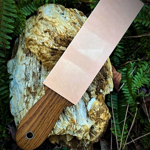 May include: A light pink leather strop with a wooden handle. The strop is resting on a piece of weathered rock.