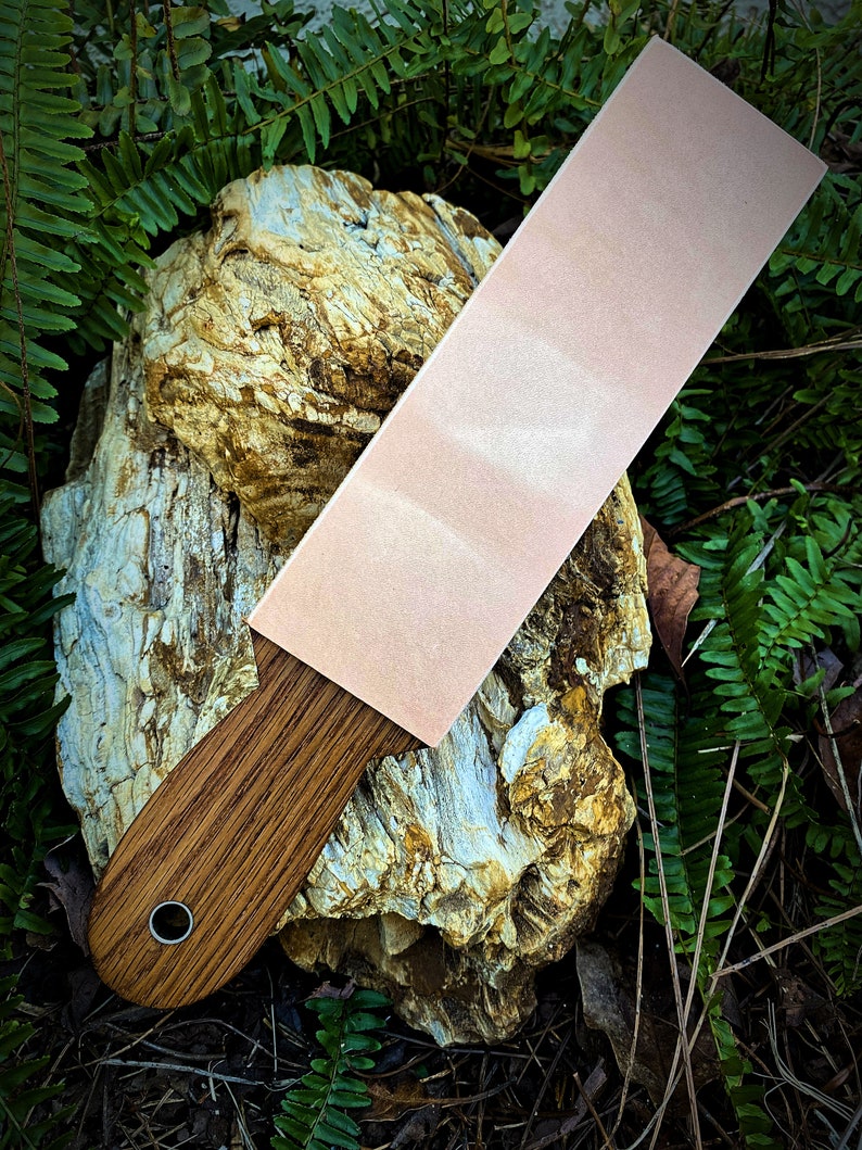 May include: A light pink leather strop with a wooden handle. The strop is resting on a piece of weathered rock.