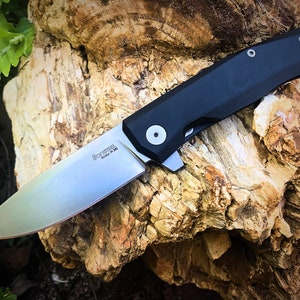 May include: A black and silver folding knife with a partially open blade. The knife has a black handle with a textured surface and a silver blade with the words "Microtech" and "Italy M-390" engraved on it.
