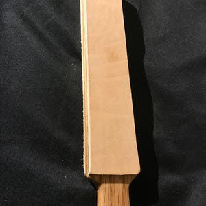 Puede incluir: Una correa de cuero marr&oacute;n con un mango de madera. La correa se utiliza para afilar navajas de afeitar.