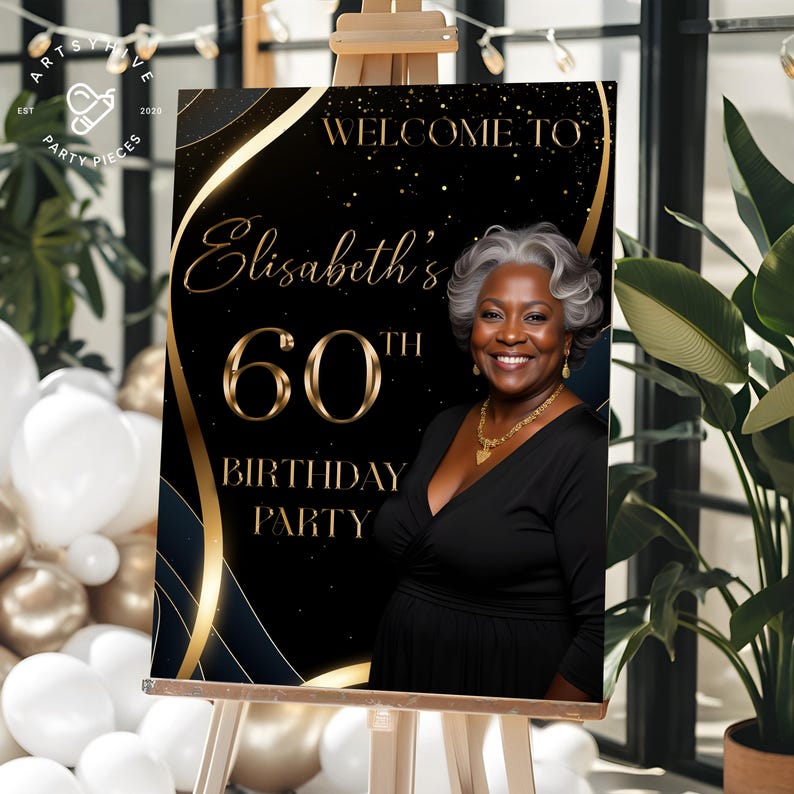 May include: A black and gold birthday party sign on an easel. The sign reads "Welcome to Elisabeth's 60th Birthday Party" with a photo of a smiling woman. The sign has gold accents and a starry background.