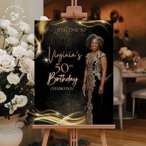 May include: A black and gold birthday celebration sign on an easel. The sign reads "Welcome to Virginia's 50th Birthday Celebration" with a photo of a woman in a black and gold dress. The sign has gold accents and is surrounded by a blurred background.