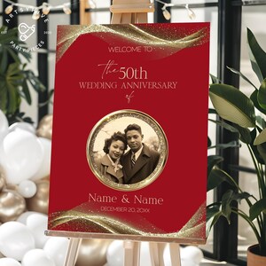 Może przedstawiać: Czerwony znak rocznicy ślubu na sztaludze. Na znaku widnieje napis "Witamy na 50. rocznicy ślubu" ze zdjęciem pary w złotej ramie. Znak zawiera również imiona i datę.