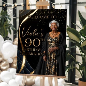 May include: A black and gold birthday celebration sign on an easel. The sign reads "Welcome to Viola's 90th Birthday Celebration" in gold script. A woman in a black and gold dress is in the image.