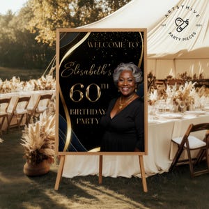 May include: A wooden easel displaying a black and gold sign that reads "Welcome to Elisabeth's 60th Birthday Party." The sign features a photo of a smiling woman and decorative gold accents. The sign is set up outdoors at a party.