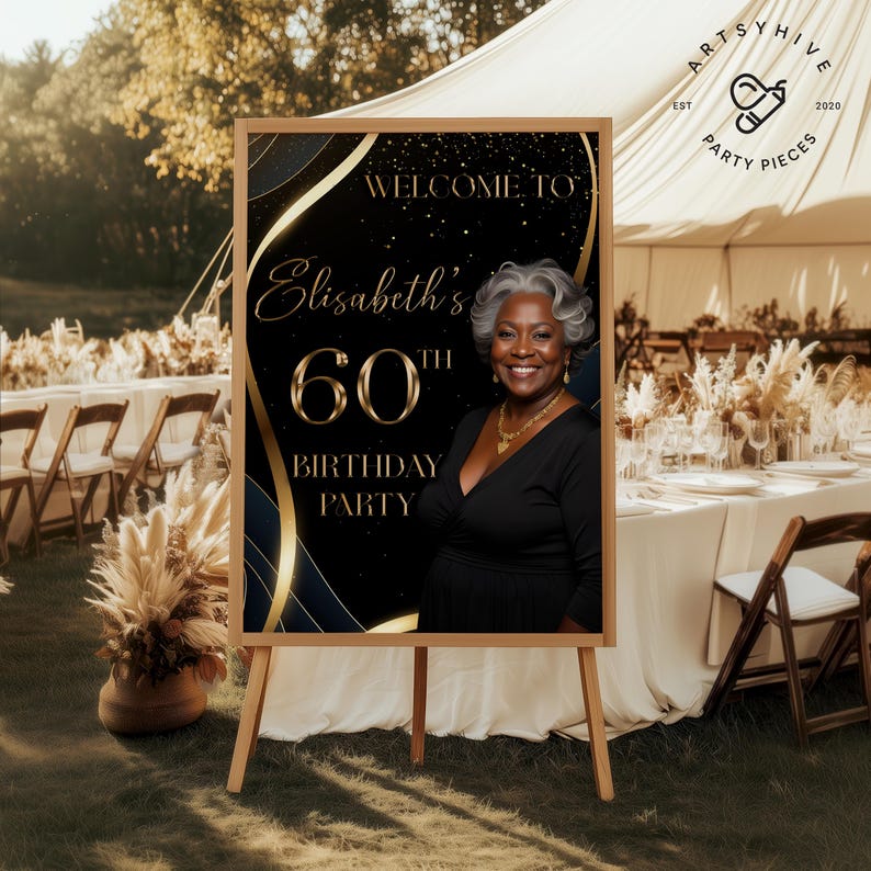 May include: A wooden easel displaying a black and gold sign that reads "Welcome to Elisabeth's 60th Birthday Party." The sign features a photo of a smiling woman and decorative gold accents. The sign is set up outdoors at a party.