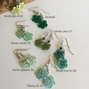 K&ouml;nnte beinhalten: H&auml;kelohrringe in Form von Blumen in verschiedenen Gr&uuml;nt&ouml;nen, darunter Hellgr&uuml;n, Mintgr&uuml;n, Dunkelgr&uuml;n und T&uuml;rkis. Die Ohrringe werden auf einer Holzoberfl&auml;che mit Textbezeichnungen f&uuml;r die Farben angezeigt.